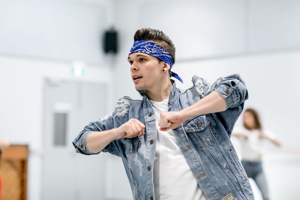 A dancer mid-movement in the studio, focused on the mirror